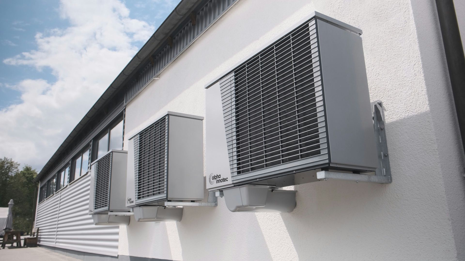 Three gray air conditioning units mounted on a white wall